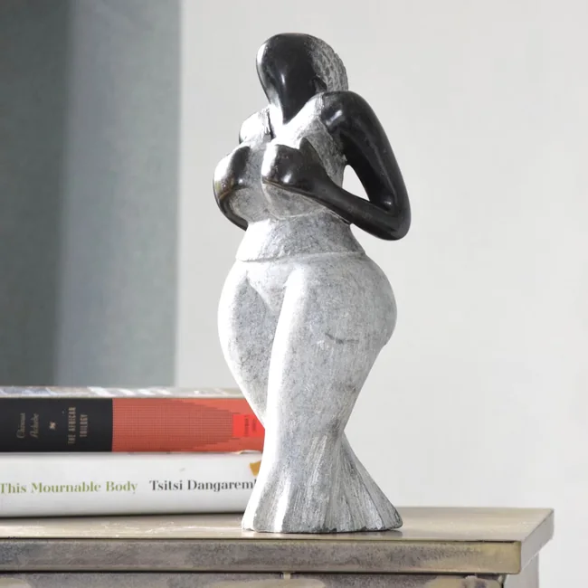 En skulptur i stein av to figurer som holder rundt hverandre, på en hylle over en bunke bøker.